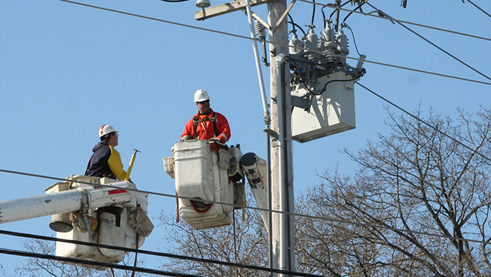 Two utility workers on cranes discussing issues with a transformer