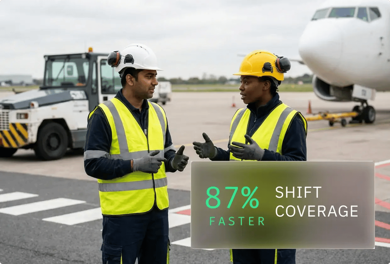 Two ground crew members, wearing safety gear and reflective vests, stand and talk on the airport tarmac with a parked aircraft and service vehicle in the background.