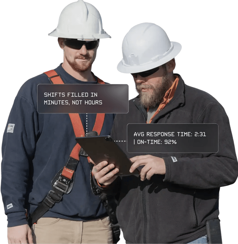 Two utility workers wearing hard hats reviewing information on a tablet while standing beside a utility truck outdoors.