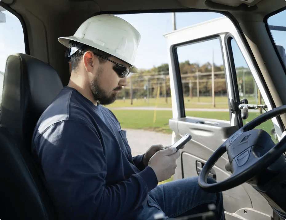 Man in hard hat using phone while sitting in vehicle.