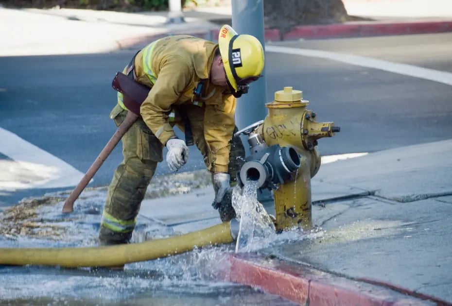 Firefighter inspecting a hydrant with water flowing out.