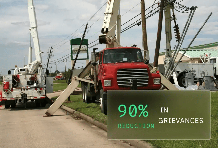 A red utility truck with aerial booms parked on grass, accompanied by a sign displaying "90% reduction in grievances."