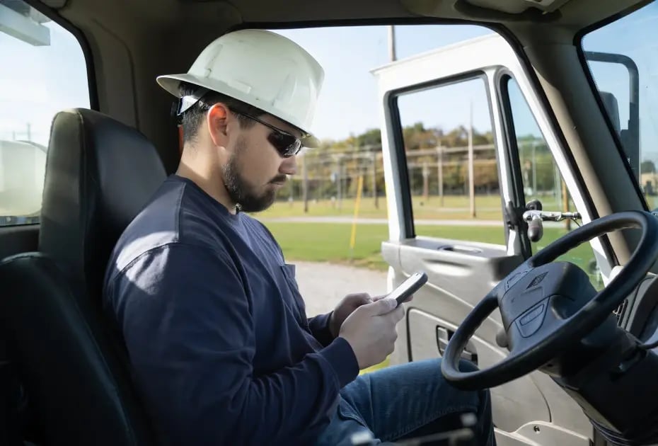 Man in hard hat using phone in truck's cab.