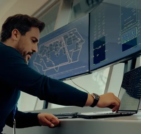 Man working at control room with multiple screens displaying data and maps.