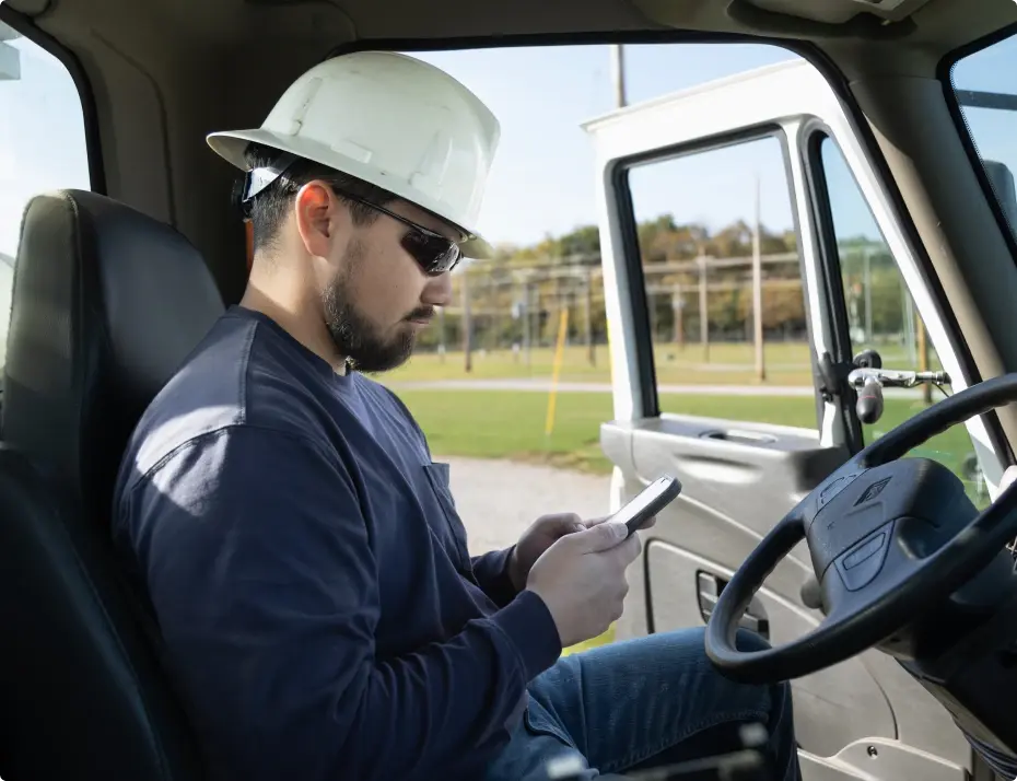 Man in hard hat using phone while sitting in vehicle.