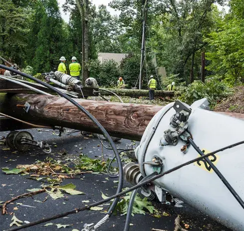Utility workers in safety gear assess damage to fallen power lines amidst debris.