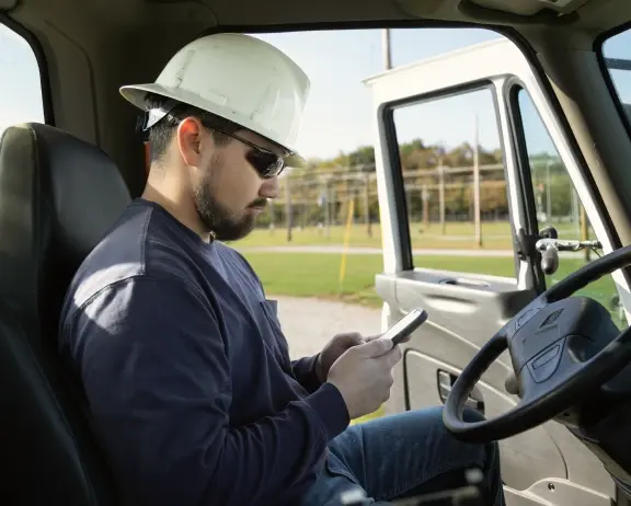 Man in hard hat using phone while sitting in truck's driver seat.