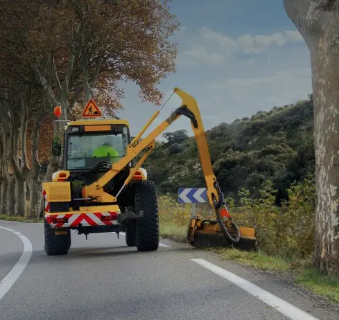 Roadside maintenance vehicle with grass cutter clearing vegetation.