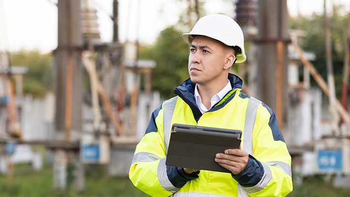 Man in a high-vis vest and a hardhat holding a tablet and looking into the distance