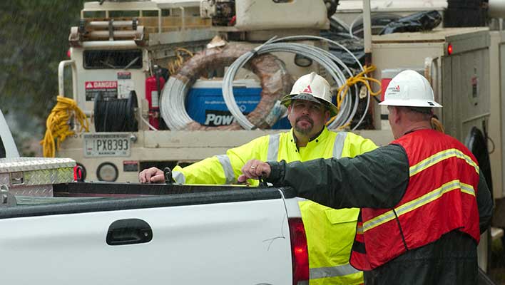 Two men in high-visibility vests talking in the rain, leaning against a truck