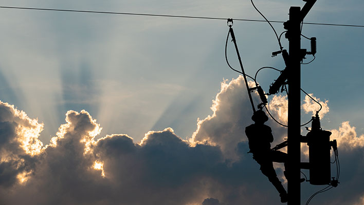 A utility worker adjusting a power line against an overcast sky