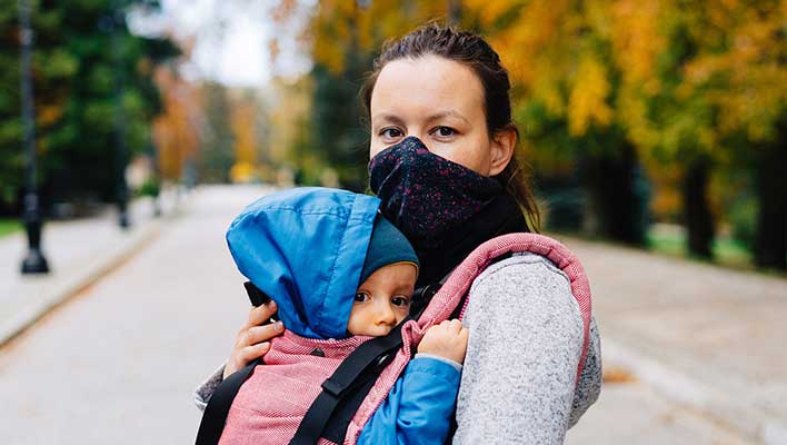 Young woman wearing a mask, holding a child, looking at the viewer