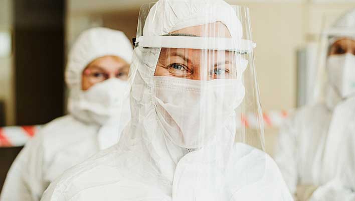 middle aged person looking at the viewer wearing a mask and face shield