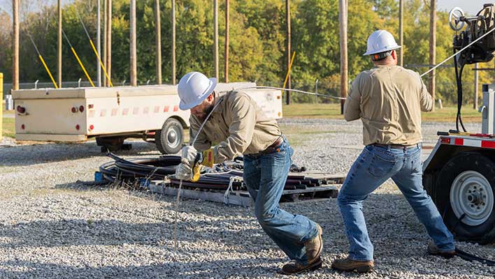 Two line workers pulling a metal wire off the back of a truck