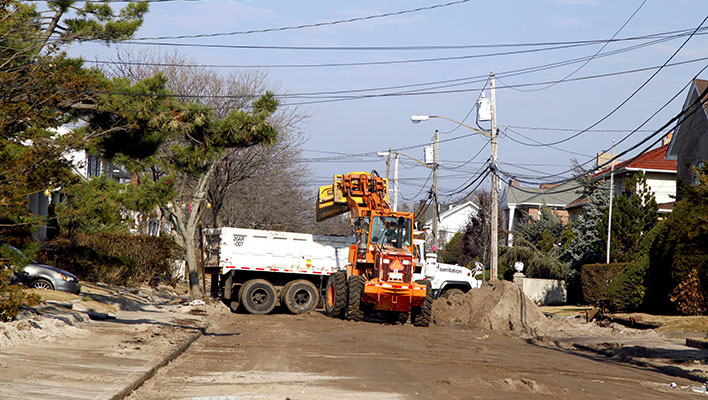 A forklift helping to move storm debris into a large garbage truck