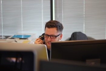 Candid picture of a man with a beard and glasses smiling while on a telephone