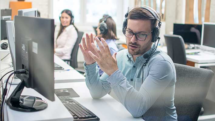 Young man with a headset, actively speaking with someone while sitting at a computer