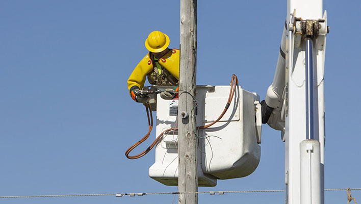 A utility worker wrapping cable around a pole