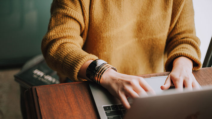 A woman typing at her laptop using the ARCOS Utility Platform to build digital reports