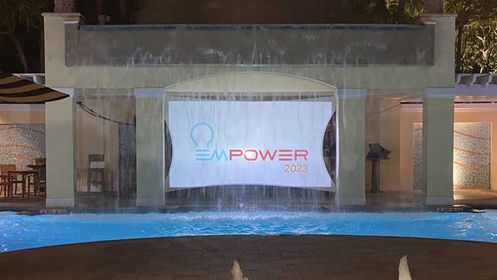 An EMPOWER 2023 Conference banner projected outside in front of a fountain