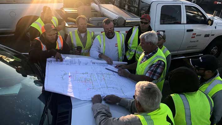 Utility workers going over plant schematics on the top of a truck's hood