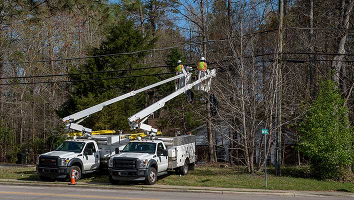 Two bucket trucks with arms extended to allow electric utility workers to inspect power lines