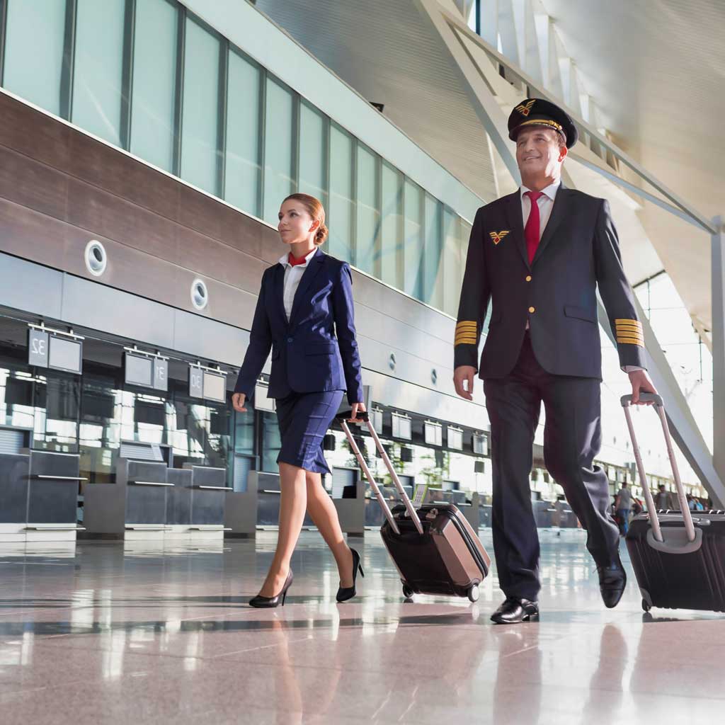 A pilot and flight attendant wheeling suitcases through an airport