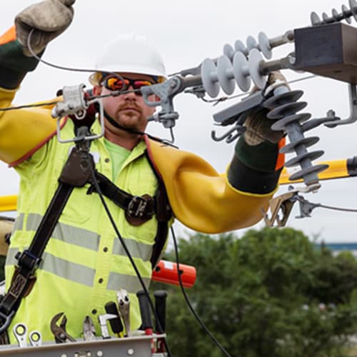 A utility crewman adding electrical line to a power pole