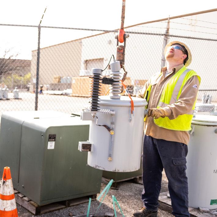 A utility worker hooking up a transformer part to be lifted by a cable