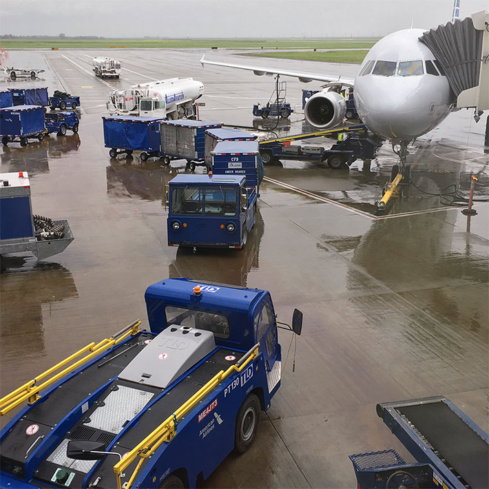 Several utility vehicles around an airplane connected to its bridge preparing for boarding