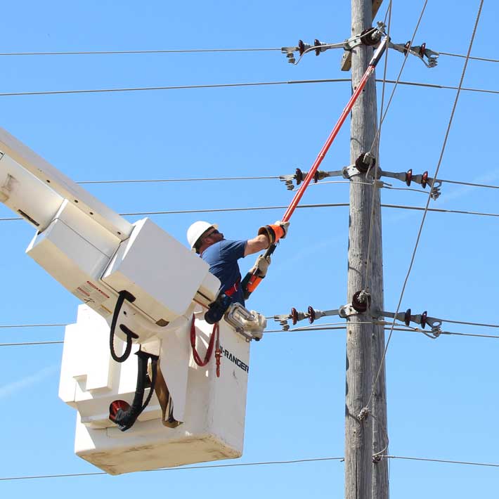 A utility working reaching up with a pole to adjust a power line