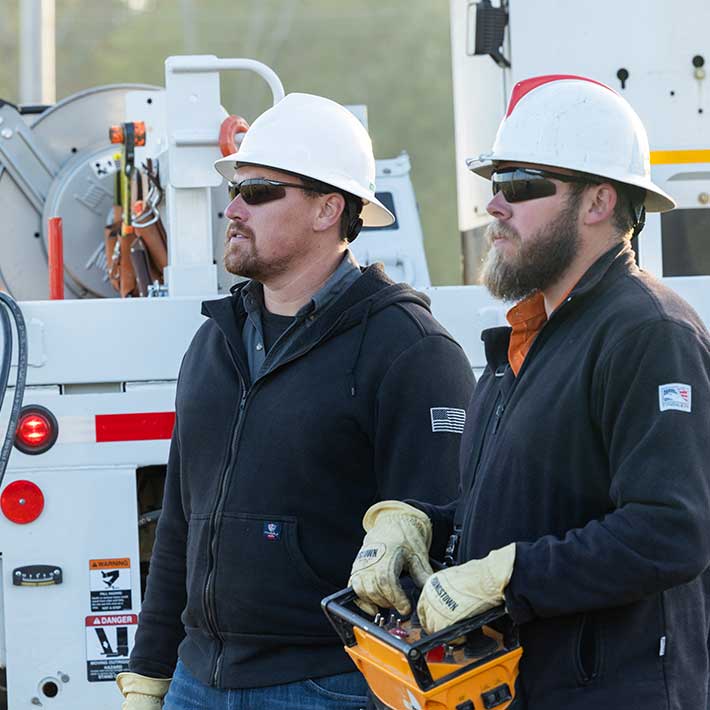 Two utility workers standing side by side operating crane controls