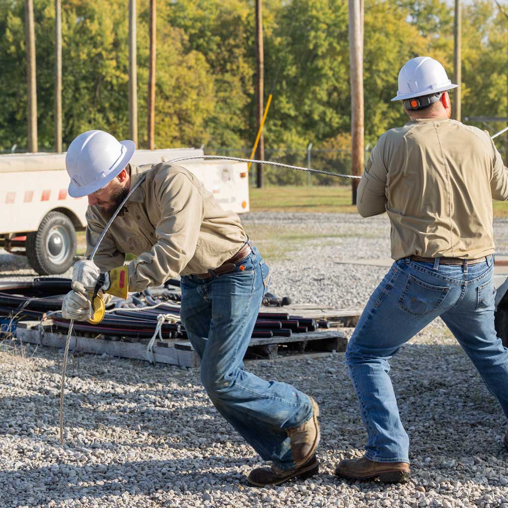 Two line workers pulling a metal wire off the back of a truck