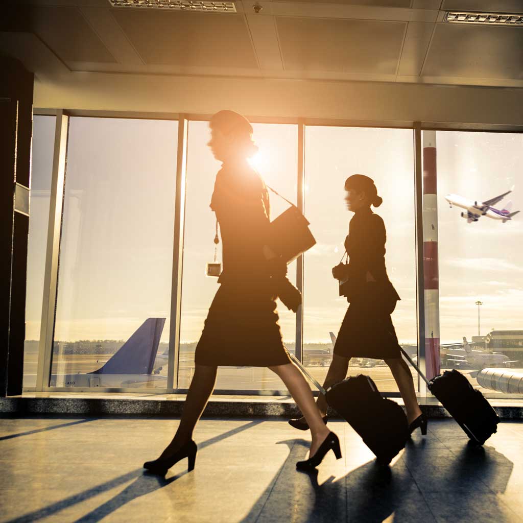 Two flight attendants wheeling luggage through an airport at sunset