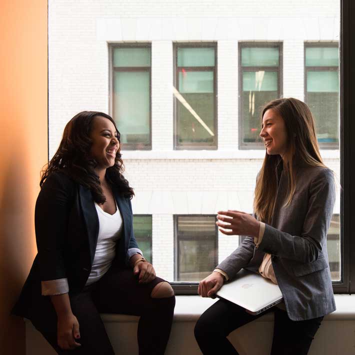 Two female ARCOS employees laughing together at a windowsill