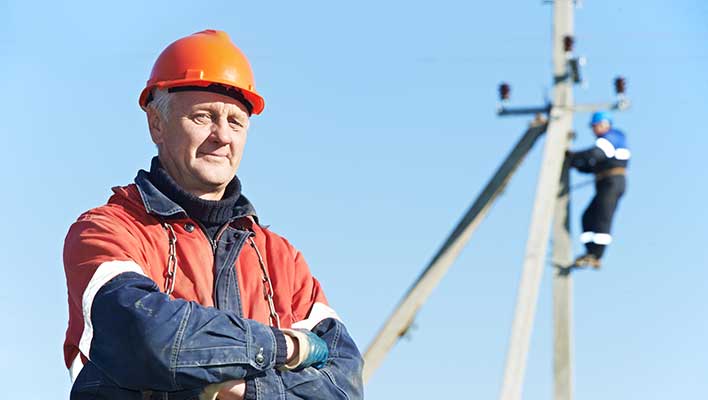 Older man with crossed arms, wearing a hard hat, looking at the viewer