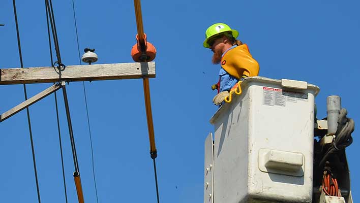 Electric utility worker in a bucket truck, inspecting a power line.