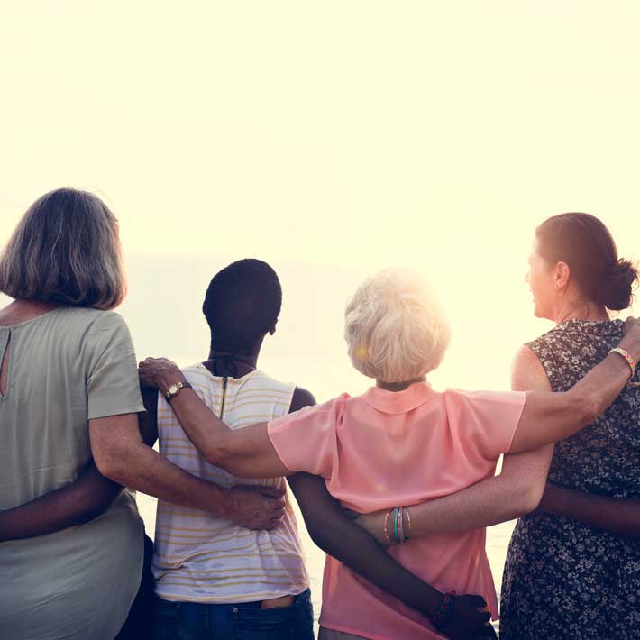 Four woman facing away from the viewer with arms around each others shoulders