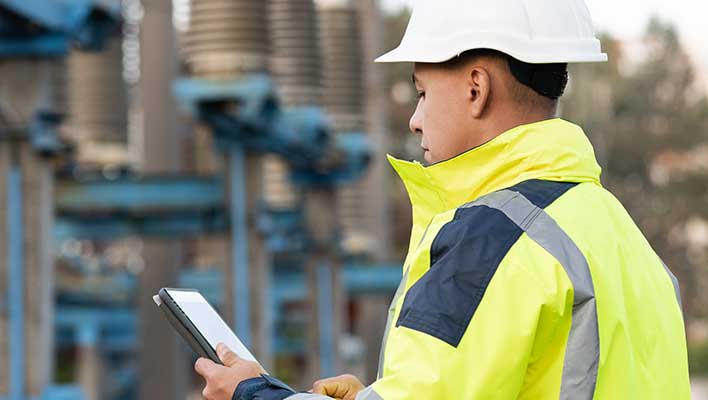 A utility worker using ARCOS utility software on a tablet to check power levels at a plant